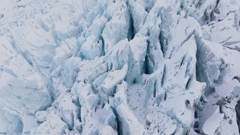 Aerial-view-over-textured-ice-formations-in-Falljokull-glacier-covered-in-snow,-Iceland