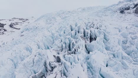 Aerial-panoramic-landscape-view-over-ice-formations-in-Falljokull-glacier-covered-in-snow,-Iceland