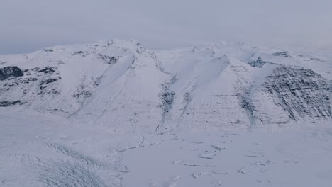 Aerial-panoramic-view-over-Skaftafellsjokull-glacier-surrounding-mountains,-in-Iceland,-covered-in-snow,-at-dusk