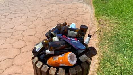 Overfilled-trash-dumpster-with-unrecycled-glass-and-plastic-bottles-by-the-beach,-people-not-recycling-garbage-in-Marbella-Spain,-4K-shot