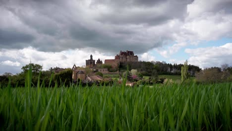Wide-angle-view-timelapse-of-Biron-castle-with-vegetation-and-flowers-in-foreground