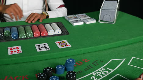 Casino-Croupier-Poker-Dealer,-Der-Eine-Ass-Karte-An-Einem-Black-Jack-Tisch-Mit-Stapeln-Von-Bargeld-Und-Chips-Austeilt