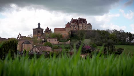 Timelapse-of-Biron-castle-with-vegetation-and-flowers-in-foreground,-Dordogne,-France
