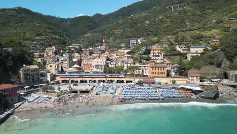 Amazing-Aerial-View-of-Monterosso,-Cinque-Terre-as-Train-Arrives-with-Tourists