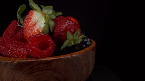 Statisch-Rotierende-Waldfrüchte-In-Einer-Holzschale-Mit-Schwarzem-Hintergrund,-Erdbeeren,-Blaubeeren,-Himbeeren,-Gesunde-Früchte,-4K-Aufnahme