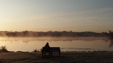 cinematic-approach-shot-of-a-woman-sat-on-a-wooden-bench-halfway-through-her-morning-run-when-the-sun-rises-to-take-in-the-scenery-and-be-present-with-life