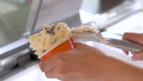 Hand-scooping-chocolate-chip-ice-cream-from-freezer-to-cup,-closeup