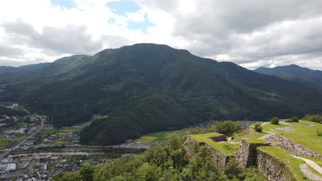 Takeda-castle-ruins-and-mountains-panoramic-view-of-green-landscape-overlooking-city-and-highway-in-a-valley