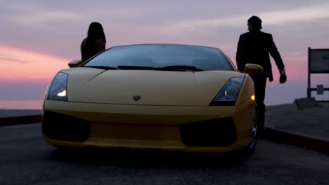 Erfolgreiches-Power-Paar-Steigt-Bei-Sonnenuntergang-Am-Strand-Aus-Seinem-Schicken-Lamborghini-Sportwagen-Aus