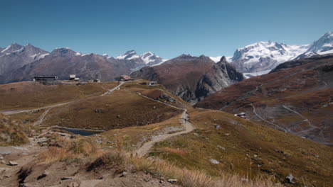 Excursionista-En-Las-Montañas-De-Los-Alpes-Junto-A-Un-Lago-Con-Teleféricos-Al-Fondo