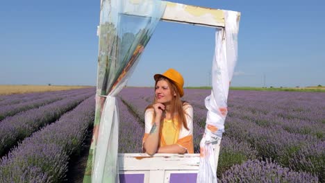 Medium-shot-of-young-woman-in-hippie-style-leaning-against-decorative-door-in-lavender-field
