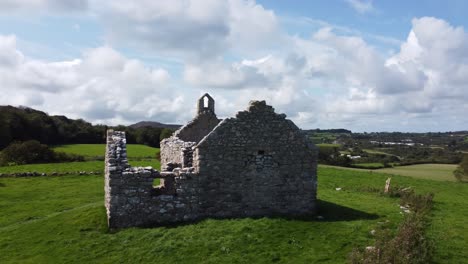 Aerial-view-circling-Capel-Lligwy-as-tourists-visit-the-ruined-chapel-on-Anglesey-island-coastline,-North-Wales-countryside