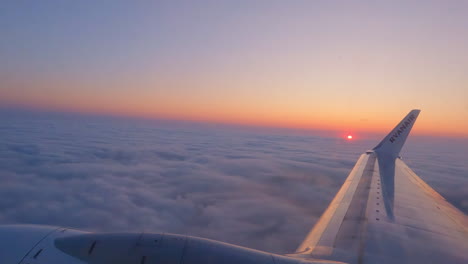 Glowing-sunrise-above-cloudscape-through-window-of-Ryanair-aircraft