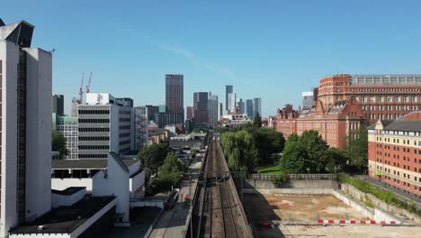 Aerial-drone-flight-along-the-train-tracks-from-Piccadilly-to-Oxford-Road-train-station,-giving-a-revealing-skyline-of-Manchester-City's-Skyscrapers