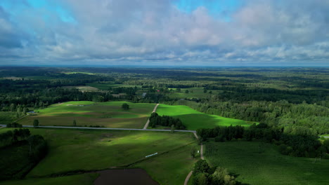 Woodland-flatlands-and-clouds-in-Latvia,-aerial-drone-ascend-over-clouds-view
