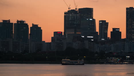 Seoul-Cruise-Tour-Ferry-Cruising-at-Sunset-Along-Han-River-With-Silhouetted-Yeouido-District-in-Background---wide-angle