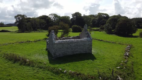 Aerial-view-circling-Capel-Lligwy-ruined-stone-chapel-on-Anglesey-island-coastline,-North-Wales
