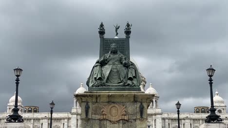 Toma-De-ángulo-Bajo-De-La-Estatua-De-La-Reina-Victoria-Sentada-Frente-Al-Monumento-A-Victoria-En-Kolkata,-India,-Con-Nubes-Oscuras-Pasando