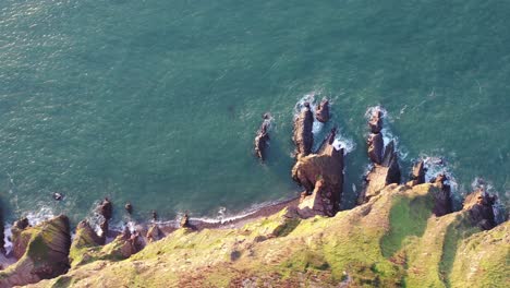Drone-shot-moving-from-left-to-right-while-looking-down-on-a-rocky-coastal-scene,-with-ocean-waves-crashing-into-rocks-on-the-North-Devon-coast-,-UK