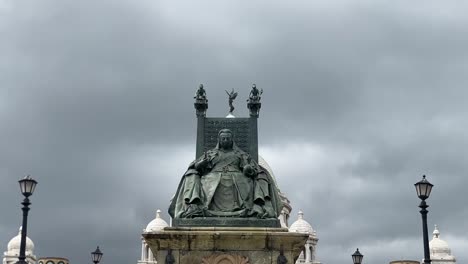Tilt-up-shot-of-statue-of-Queen-Victoria-sitting-in-front-of-Victoria-Memorial-in-Kolkata,-India-on-a-cloudy-day