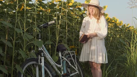 Girl-on-bike-ride-stops-to-read-book-in-solitude-of-evening-sunflower-field