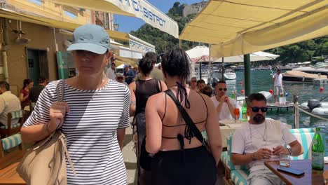 Tourists-explore-and-enjoy-sitting-by-the-restaurants,-having-drinks,-and-people-watching-during-the-summertime-holidays-in-Portofino,-Italy