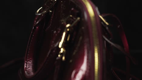 Dark-red-glossy-Louis-Vuitton-handbag-turning-with-black-dark-background,-expensive-luxury-product-made-of-leather,-4K-shot