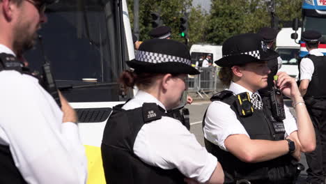 A-unit-of-Metropolitan-police-officers-stand-by-a-police-van-while-monitoring-a-protest-on-a-bright-and-hot-sunny-day