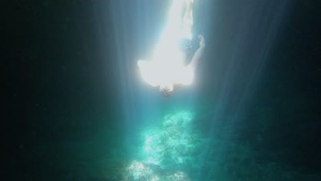 A-diver-is-thoroughly-enjoying-his-underwater-adventure,-completely-immersed-in-the-mesmerizing-spectacle-of-sunlight-casting-stunning-illusions-through-the-pure,-crystalline-water