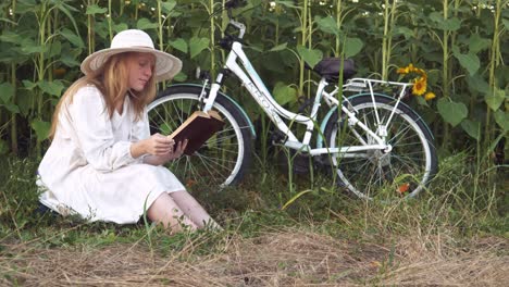 Das-Weiße-Kleid-Des-Mädchens-Stoppt-Die-Radtour,-Um-In-Der-Einsamkeit-Ländlicher-Sonnenblumen-Ein-Buch-Zu-Lesen