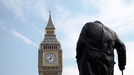 Un-Avión-Privado-Vuela-Detrás-De-La-Estatua-De-Winston-Churchill-En-La-Plaza-Del-Parlamento-Y-La-Torre-Isabel-En-El-Palacio-De-Westminster,-Que-Alberga-La-Campana-Del-Big-Ben-En-Un-Día-Brillante-Y-Caluroso