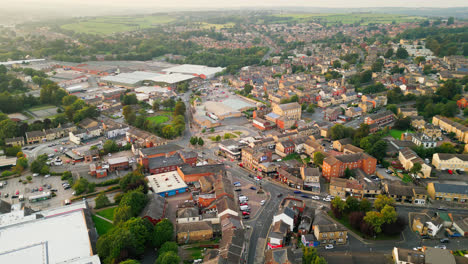 A-drone-records-Heckmondwike,-UK,-with-industrial-buildings,-bustling-streets,-and-the-old-town-center-on-a-summer-evening
