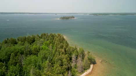 Aerial-flyover-forested-coastline-looking-out-to-water-and-islands,-Michigan