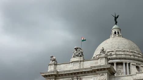 Low-angle-shot-of-Indian-flag-flying-on-top-of-Victoria-Memorial-in-Kolkata,-West-Bengal,-India-with-dark-clouds-in-the-background-during-evening-time