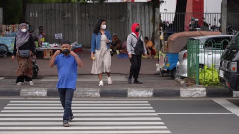 A-man-wearing-a-mask-while-crossing-the-road-in-front-of-officers-at-Senen-Station,-Jakarta