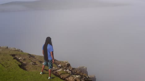 Man-gazing-into-foggy-horizon,-standing-on-cliff