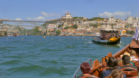 Tugboat-Followed-By-Tourist-Boat-Sailing-Over-Douro-River-With-Dom-Luís-I-Bridge-In-Porto,-Portugal