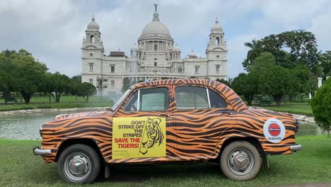 Wunderschöne-Aufnahme-Eines-Gelben-Taxis,-Das-Für-Das-Schutzprogramm-Für-Tiger-Wirbt,-Mit-Blick-Auf-Das-Victoria-Memorial-Im-Hintergrund-In-Kalkutta,-Indien,-An-Einem-Bewölkten-Tag