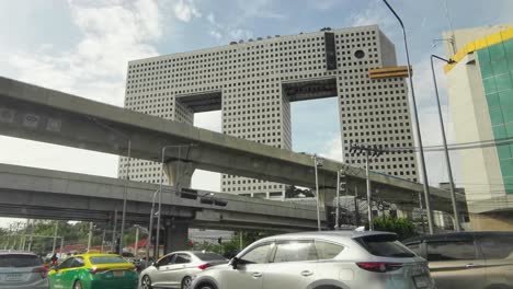 Elephant-Building-with-the-BTS-Skytrain-Traveling-Along-the-Monorail-with-Traffic-in-the-Foreground-at-Ratchayothin,-Bangkok,-Thailand
