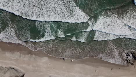 Langsame-Luftaufnahmen,-Die-über-Die-Strandküste-Fliegen,-Mit-Einem-Überblick-über-Die-Wellen,-Die-Im-Sand-Krachen