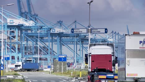 Container-trucks-enter-Rotterdam-harbor,-panorama-view-with-huge-cranes