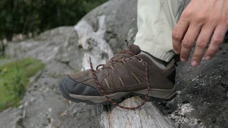 Man-tying-hiking-shoe-laces-on-hike-in-nature