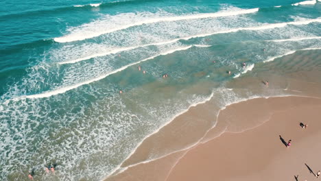 Eine-Beeindruckende-Luftaufnahme,-Die-Die-Pracht-Der-Am-Strand-Brechenden-Wellen-Aus-Einer-Majestätischen-Perspektive-Einfängt-Und-Die-Dynamische-Schönheit-Der-Küstenszene-Zeigt