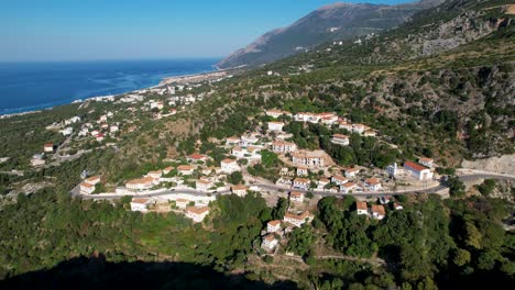 Ionian-sea-coastline-in-Albania-with-beautiful-villages-full-of-tourists-for-summer-vacation,-resorts-and-hotels-on-hills-above-blue-sea-horizon