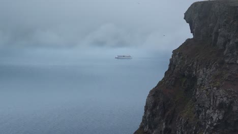 Aerial-wide-shot-of-cruise-ship-on-fjord-water-during-cloudy-day-on-Iceland-Island-with-steep-cliffs