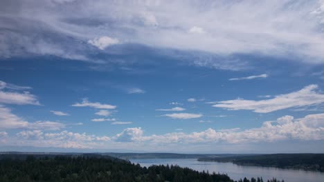 High-cirrus-clouds-slowly-move-across-a-brilliant-blue-sky,-reflecting-off-calm-waters,-aerial-hyper-lapse