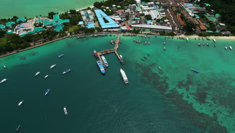 Boats-at-Koh-Phi-Phi-Don-island-harbour,-popular-tourist-destination-in-Thailand,-aerial-revealing-shot