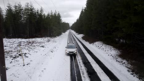A-single-white-Subaru-Crosstrek-slowly-drives-along-a-snow-covered-back-road,-aerial-track
