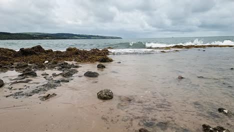 Meereswellen-In-Zeitlupe-Hinterlassen-Transparentes,-Klares-Wasser-über-Der-Sandigen-Küste-Von-Anglesey