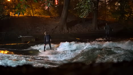 Cinematic-fade-slow-motion-Eisbach-Wave-River-Surfer-community-Munich-Germany-ground-level-zoomed-in-fall-autumn-beautiful-night-surfing-high-flow-water-surf-Upper-Bavaria-Alps-flow-follow-movement